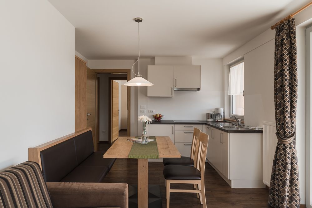 Moderne Küche mit Holz-Esstisch, Stühlen und beiger Sitzbank, Vorhängen und Hängelampe