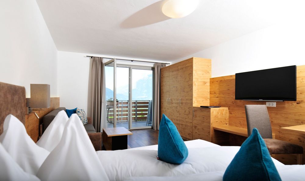 Modern ausgestattetes Hotelzimmer mit Bett, Fernseher, Sofa und Balkon mit Bergblick