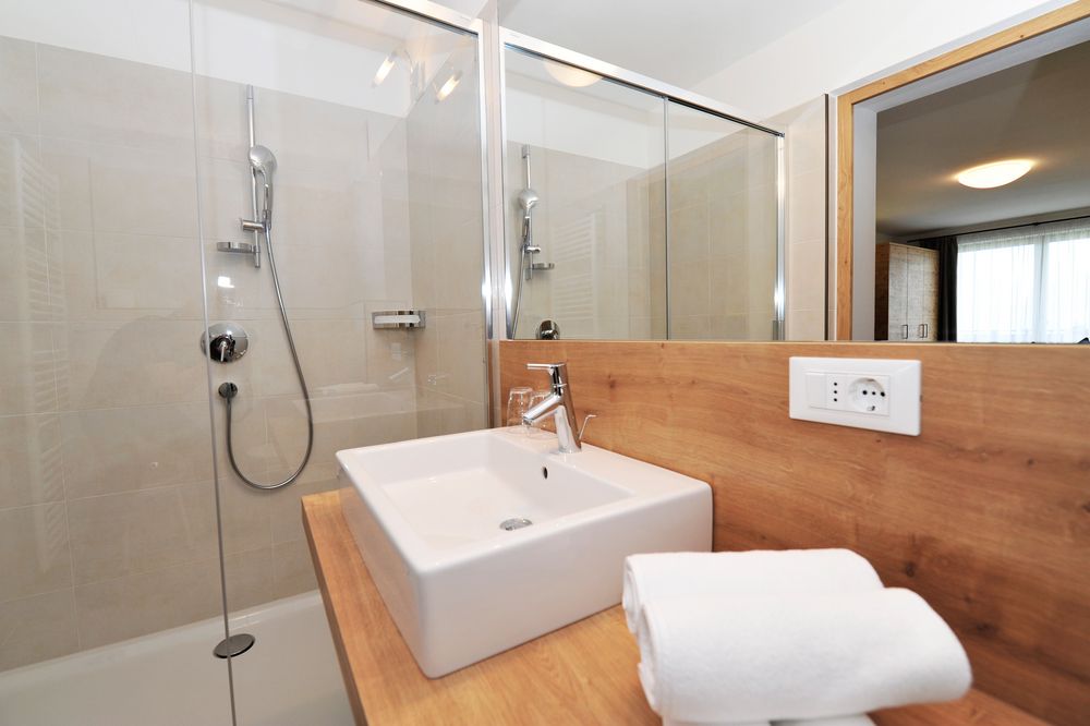 Modernes Badezimmer mit Dusche, Waschbecken und Handtüchern auf Holzarbeitsplatte