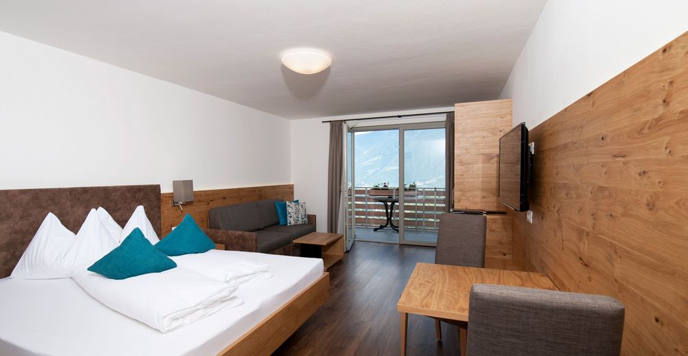 Modernes Hotelzimmer mit Doppelbett, Sofa, Holzmöbeln und Balkon mit Bergblick.