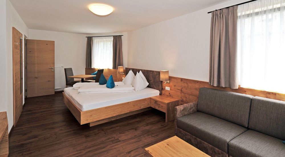 Modernes Hotelzimmer mit Doppelbett, grauem Sofa und Holzmöbeln