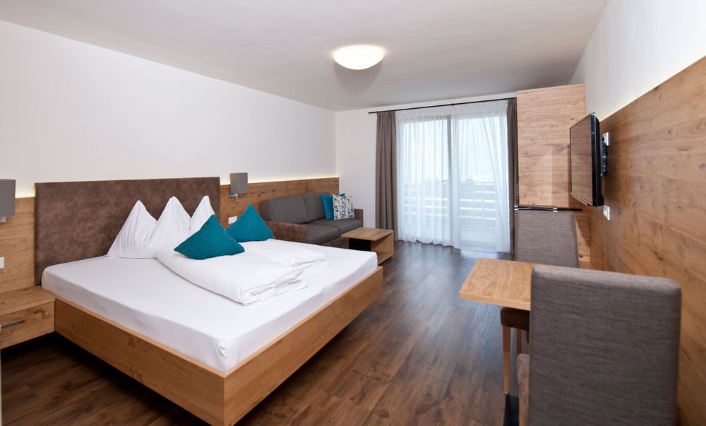Modern eingerichtetes Hotelzimmer mit Doppelbett, Sofa, Tisch und großem Fenster mit Gardinen