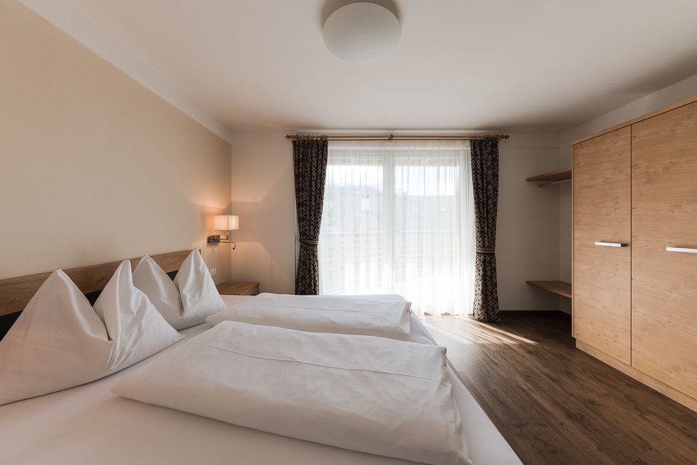 Helles Schlafzimmer mit Doppelbett, Holzmöbeln und großem Fenster mit Vorhängen