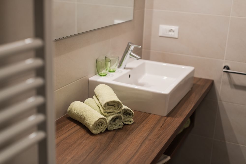 Sauberer Waschbeckenbereich mit aufgerollten Handtüchern auf einer Holzablage im Badezimmer