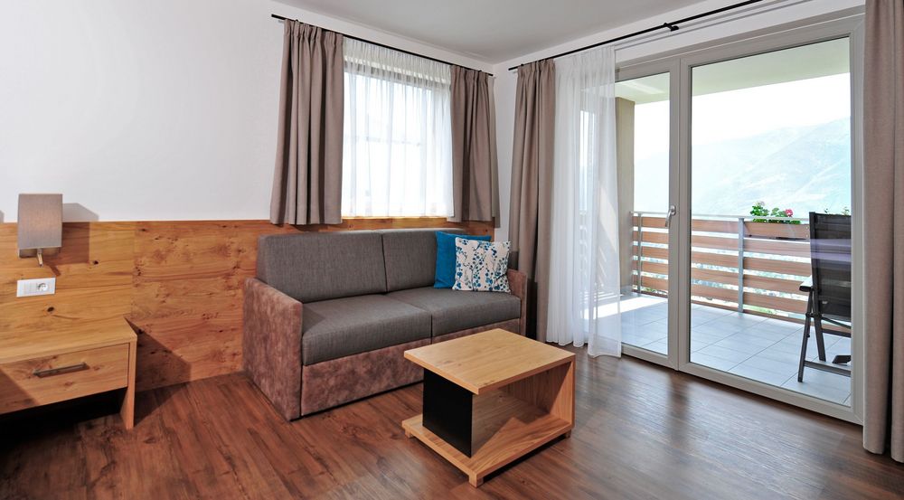 Modernes Wohnzimmer mit Sofa, Vorhängen und Balkon mit Bergblick.